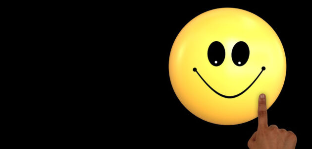 Gelber Smiley auf schwarzem Hintergrund. Ein Finger zeigt von unten rechts auf das Emoji.