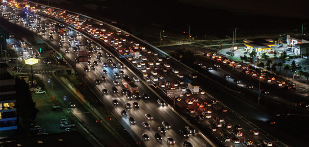 Es ist Nacht. Auf einer mehrspurigen Autobahn stehen viele Autos im Stau. Das Bild ist von oben aus der Perspektive. Sichtbar sind hauptsächlich die Lichter der Autos.
