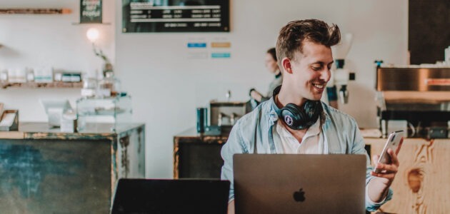 Lachender junger Mensch vor Computer in hippem Cafe