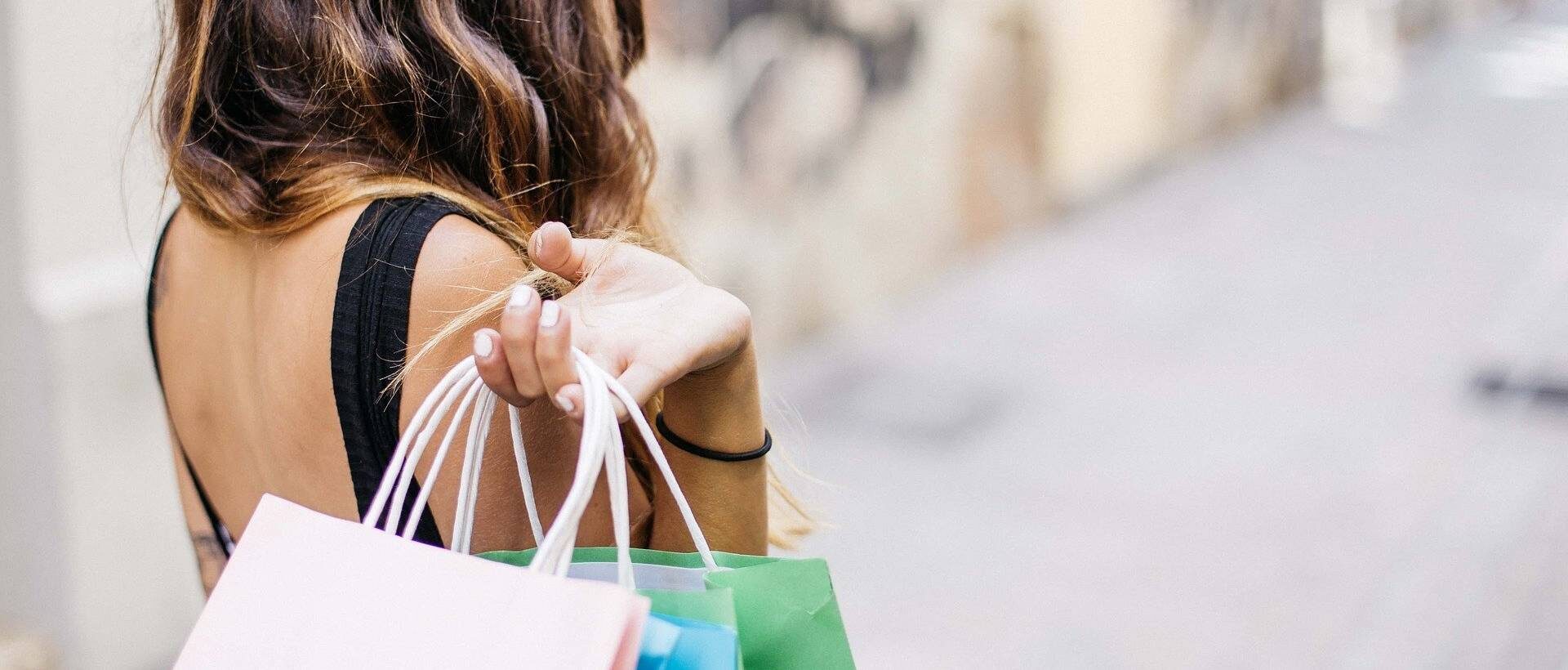 Eine Frau hält verschiedene Einkaufstüten über der Schulter, was sinnbildlich für die Shopping-Erfahrung steht.