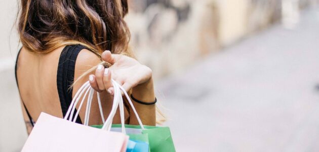 Eine Frau hält verschiedene Einkaufstüten über der Schulter, was sinnbildlich für die Shopping-Erfahrung steht.