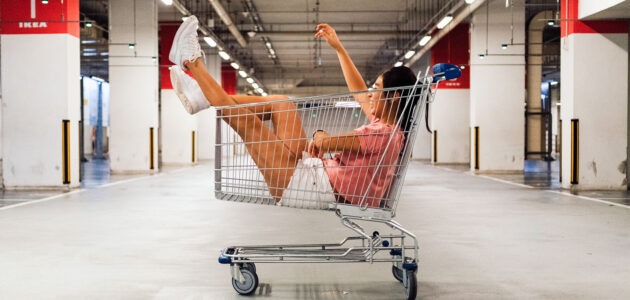 Lachende Frau in einem Einkaufswagen in einer Tiefgarage sinnbildlich für Online Shopping