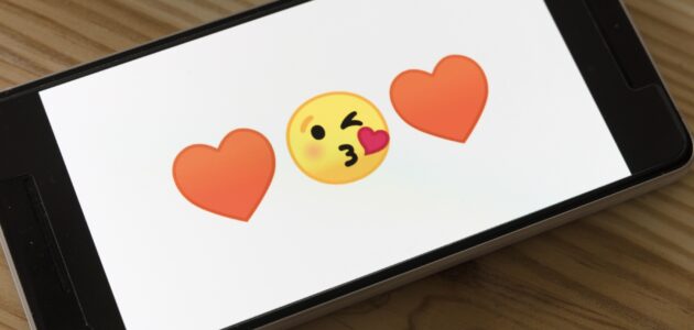 Ein Smartphone, auf dessen Bildschirm zwei Herz- und ein Kussmundemoji zu sehen sind. Dies soll das Online-Dating per Smartphone-App symbolisieren.