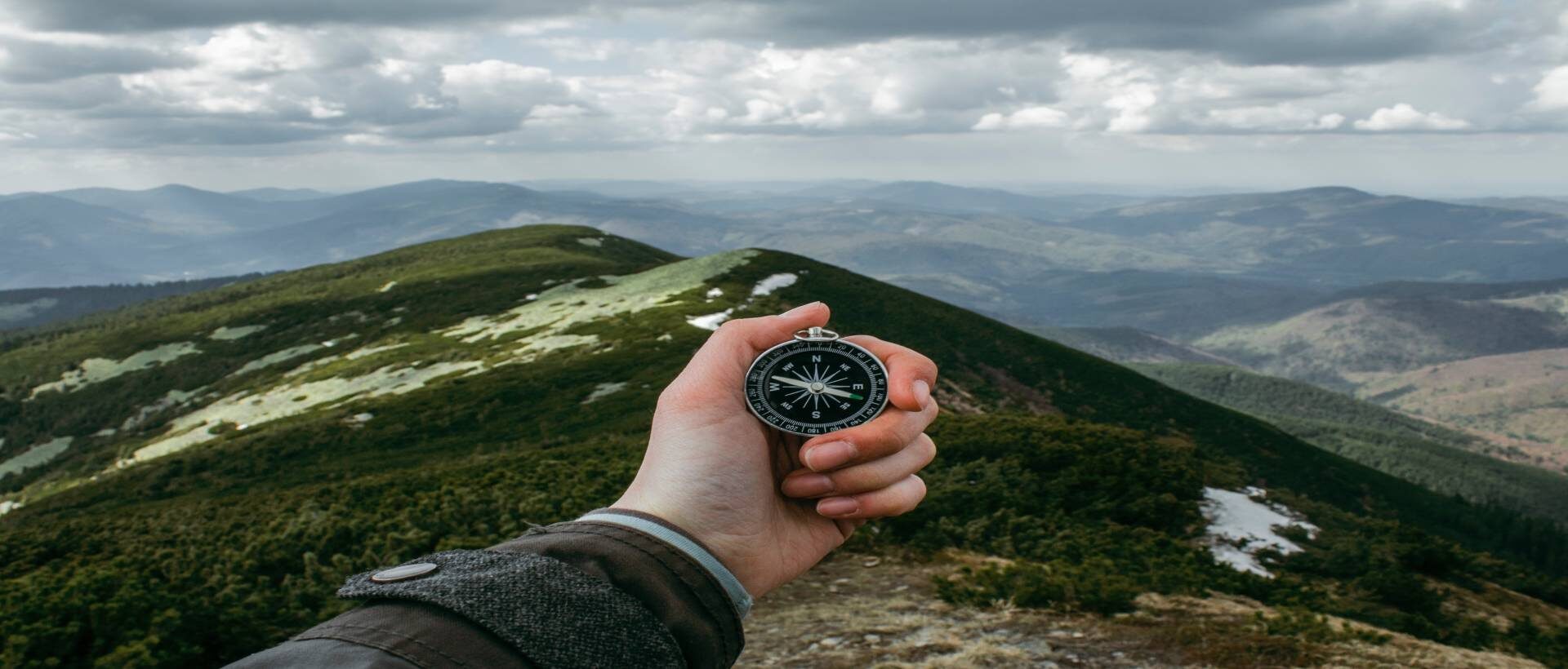 Eine Hand die einen Kompass hält, mit einer Berglandschaft im Hintergrund
