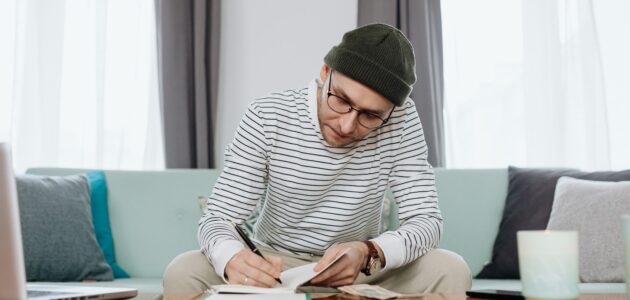 Mann sitzt auf einem Sofa und schreibt Gedanken rund um einen Business Case in sein Notizbuch
