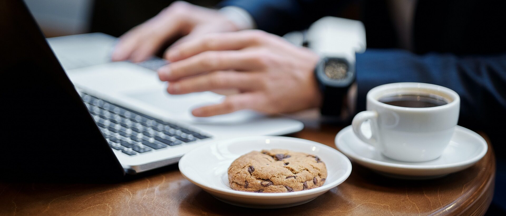 Mann schreibt am Laptop mit Kaffee und Cookie daneben