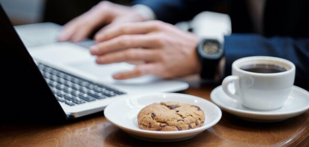 Mann schreibt am Laptop mit Kaffee und Cookie daneben