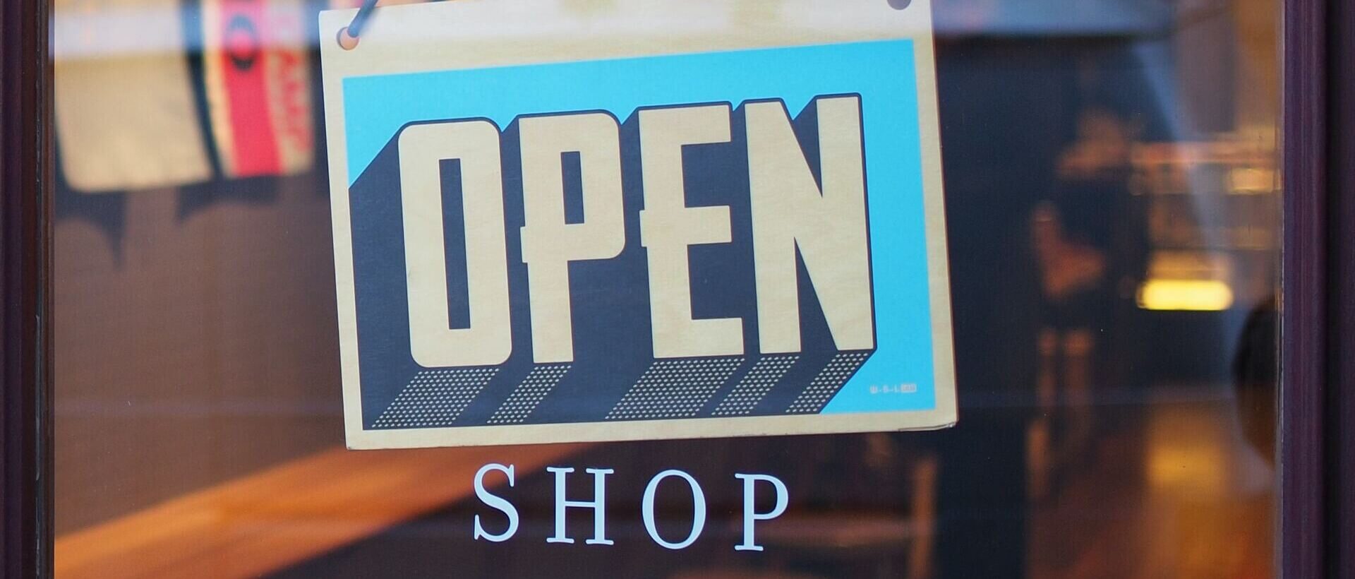 Ein Schild mit der Aufschrift "OPEN SHOP" hängt an einer gläsernen Ladentür
