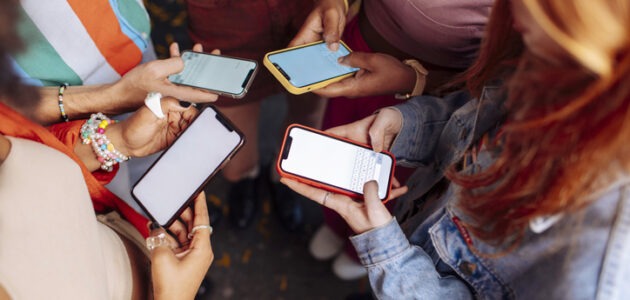 Eine Gruppe junger Menschen steht eng zusammen und tippt auf ihre Smartphones. Das Bild symbolisiert digitale Kommunikation und den Einsatz von Jugendsprache in der Werbung.