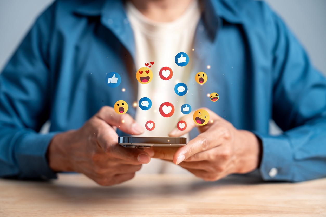 Eine Person hält ein Smartphone, über dem Symbole für Likes, Herzen, Kommentare und verschiedene Reaktionen schweben. Das Bild symbolisiert den Austausch auf der Imageboard-Plattform pr0gramm.